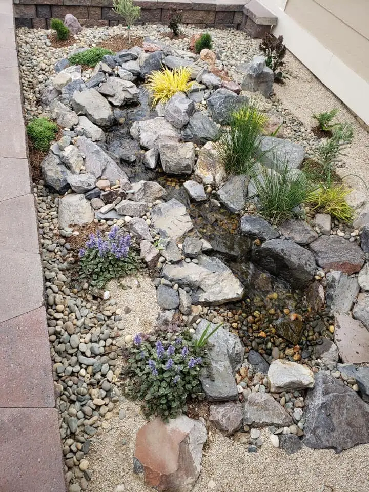 A rock stream bed with flowering plants along a side yard