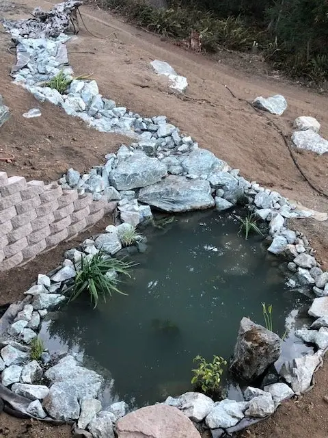 A pond liner laid in a freshly dug pond with stones being set around the edge