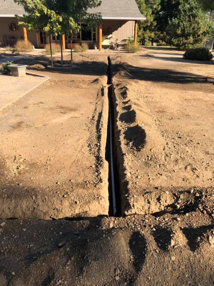 Fresh trenches with irrigation pipe being laid across a dirt yard