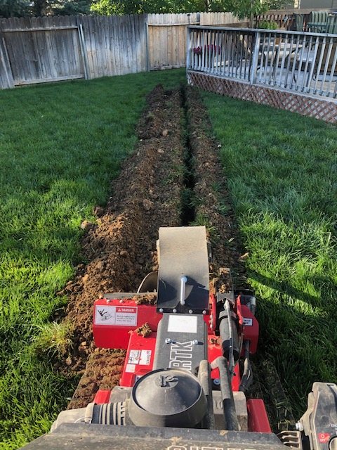 A trenching machine cutting a line across a lawn