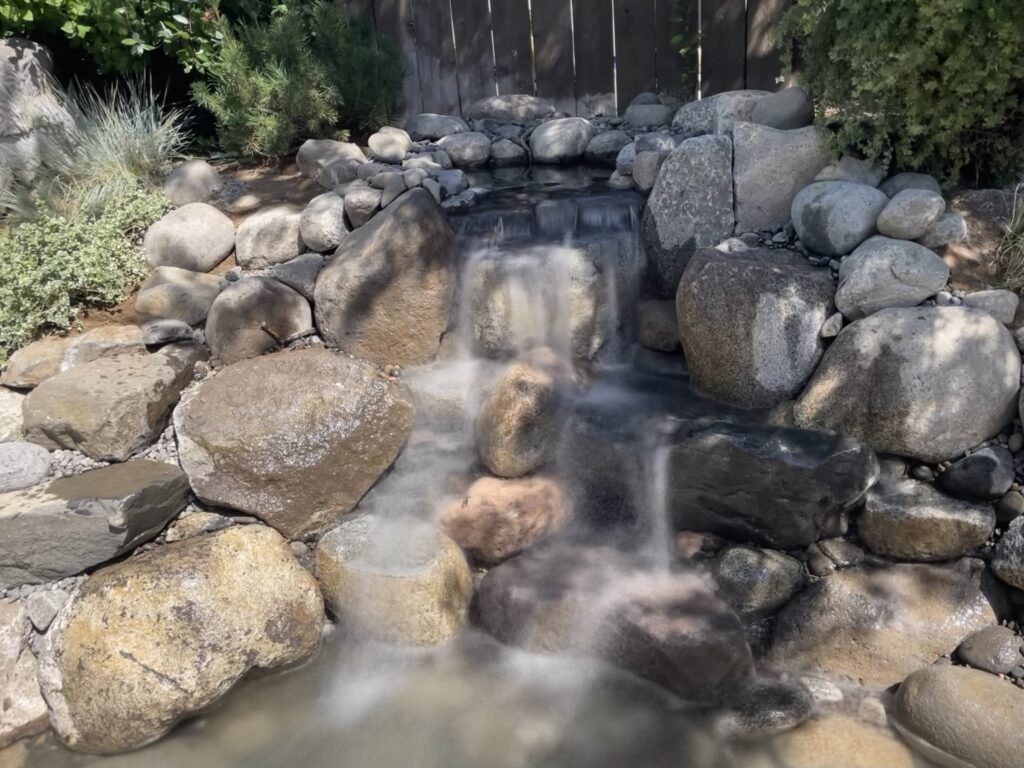 A soft waterfall tumbling between large boulders into a pond