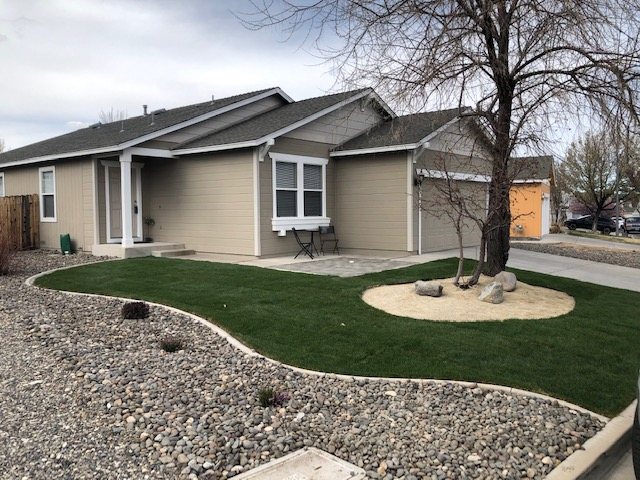 A front yard with a curved lawn and a rock bed beside a gray house
